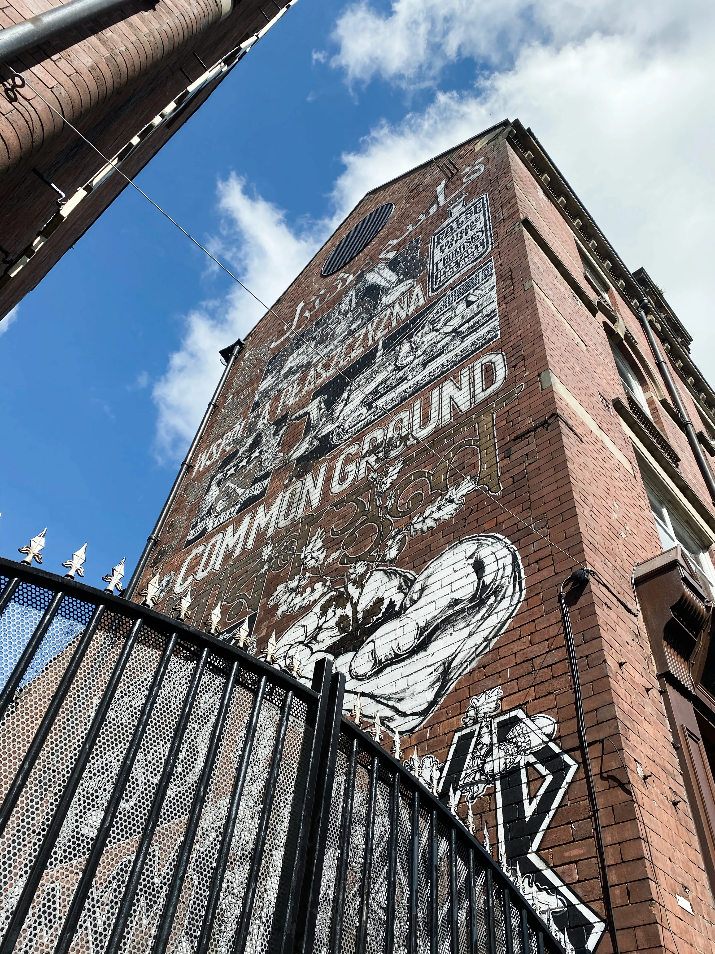 The Common Ground mural on a tall brick building, seen looking up from behind an iron gate.