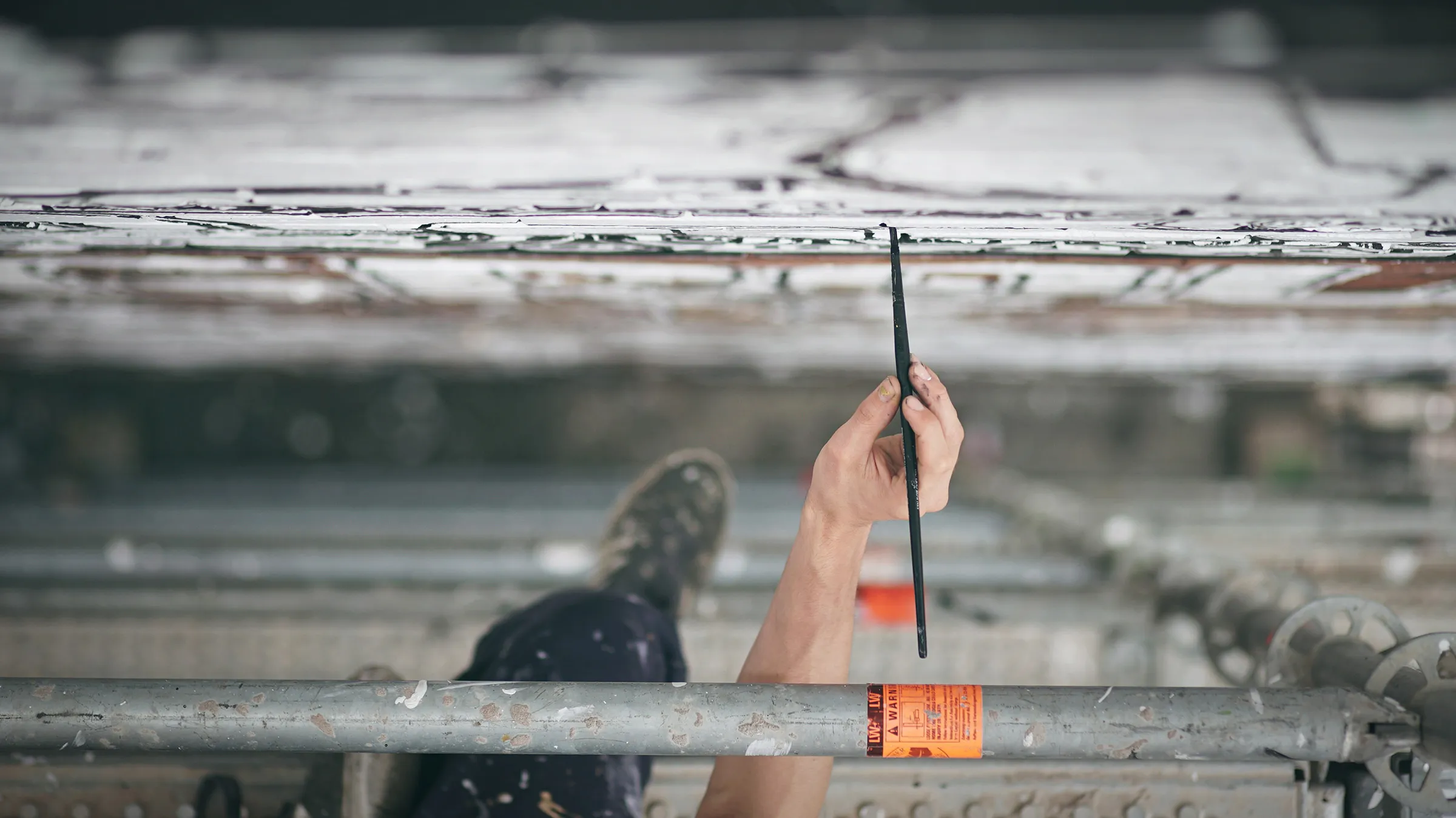 Looking up from the scaffold: a hand reaching a brush up to the wall.