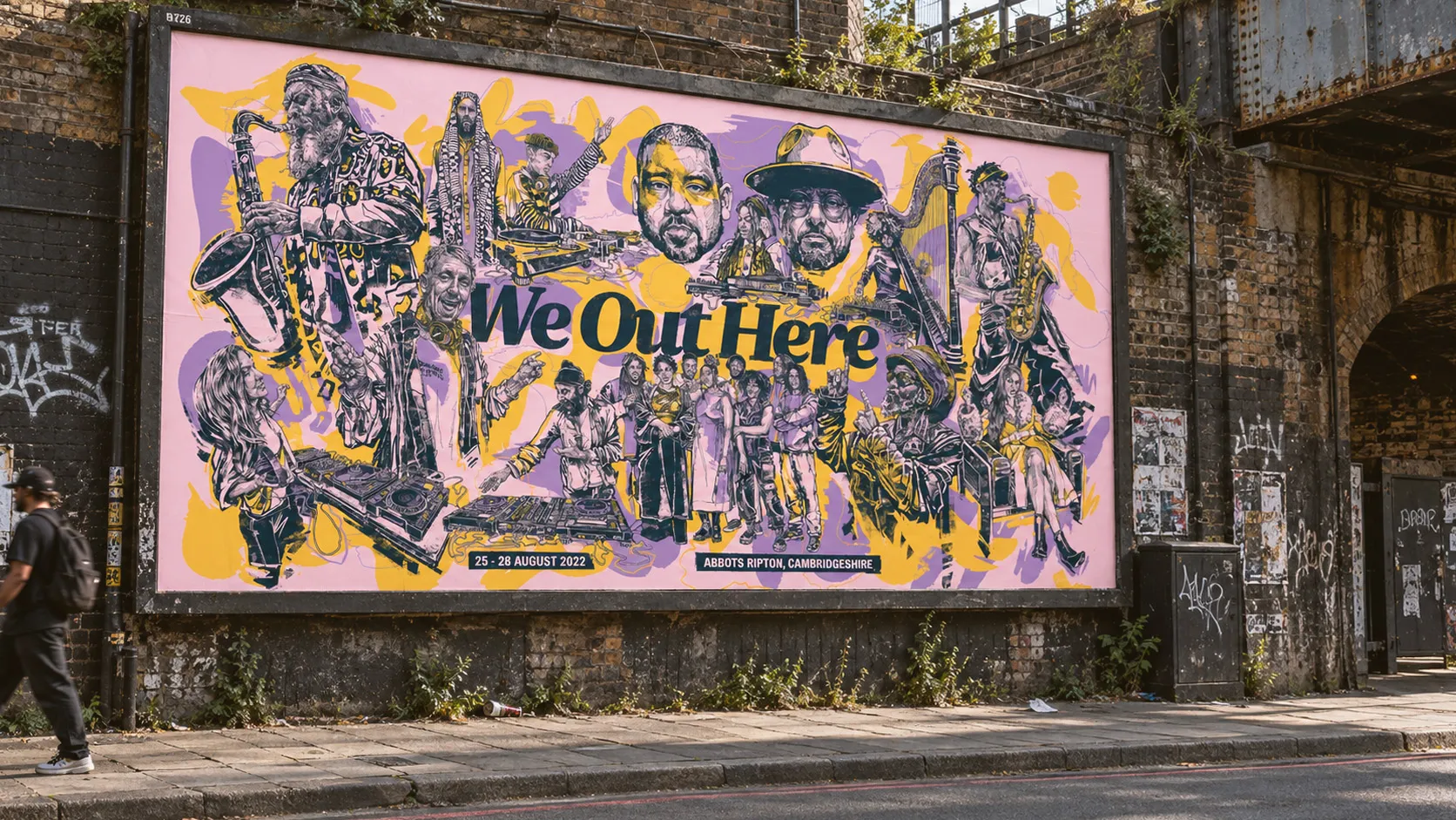 A pink and yellow We Out Here billboard covered in drawn artists, on a brick wall under a railway arch.