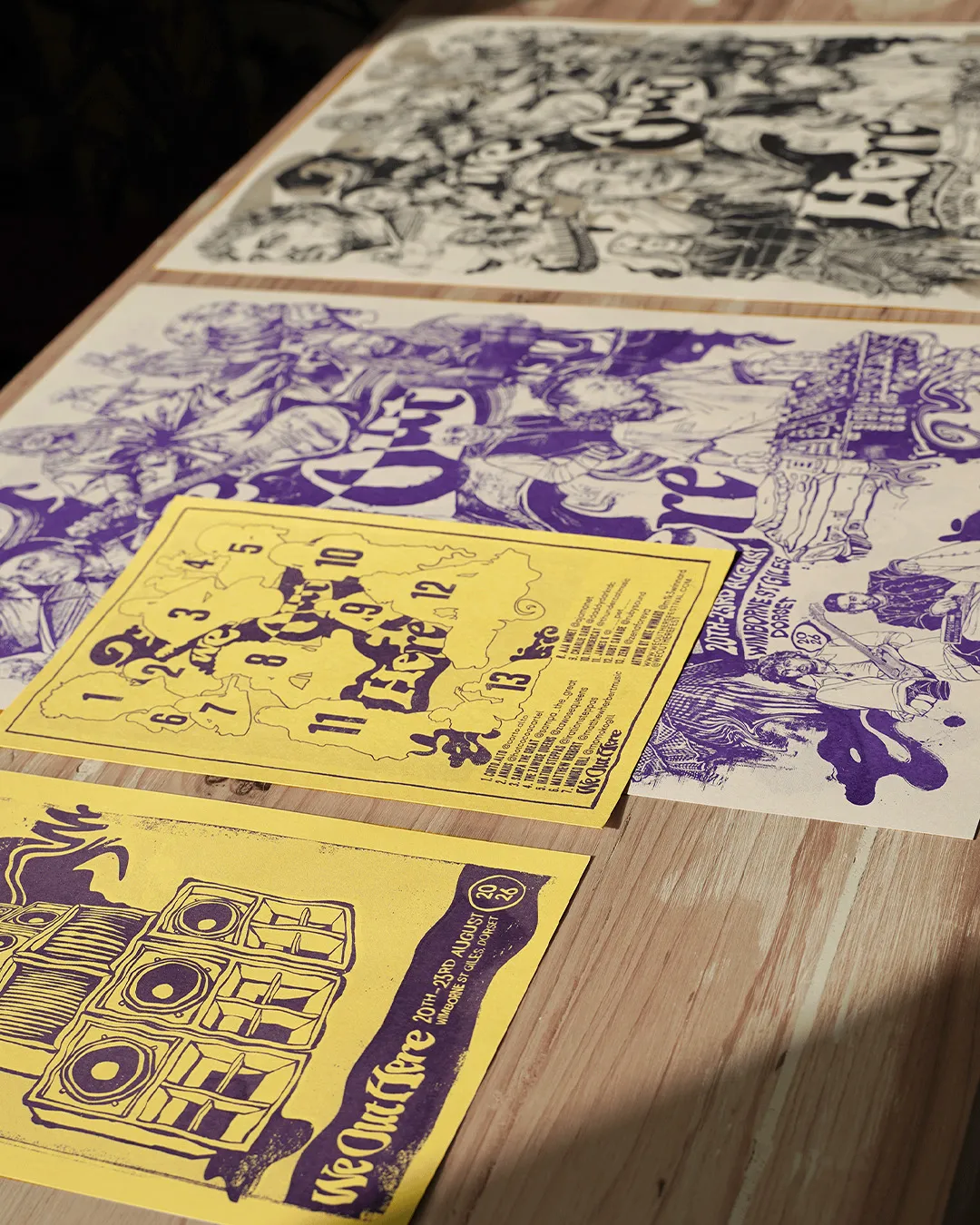 Yellow and purple risograph prints laid out on a wooden table in the sun.