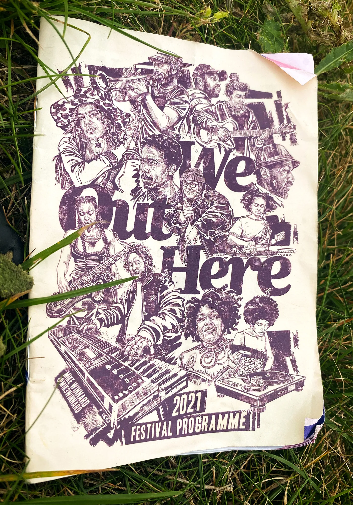 The 2021 festival programme, its cover drawn in purple, lying in long grass.